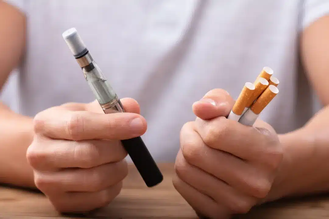 Man,Holding,Vape,And,Tobacco,Cigarette,Over,Desk